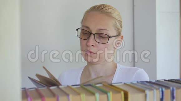 图书馆里戴眼镜的女人正在书架上的书中搜寻视频的预览图