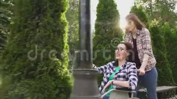 穿衬衫的女孩陪着公园里坐轮椅的女孩他们互相交流视频的预览图