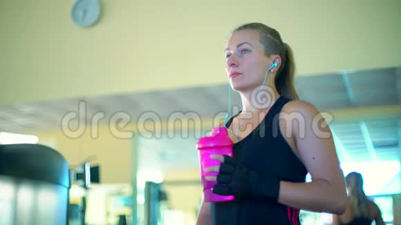 健身年轻妇女戴着防护手套和耳机喝水休息和听音乐视频的预览图