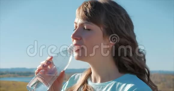 欧洲的女人出现在露天的饮料水从瓶子对抗一个晴朗的蓝天健康的生活方式视频的预览图