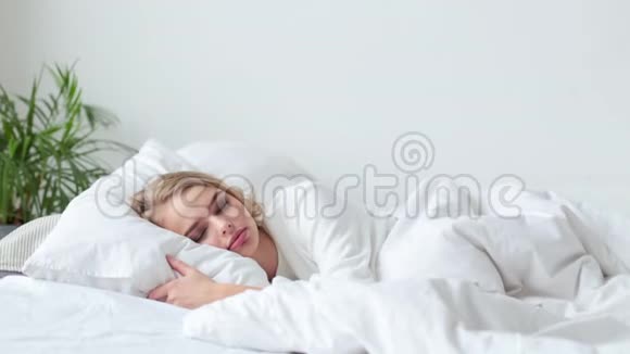 美丽的女人在卧室的床上醒来她伸展着身体微笑着视频的预览图