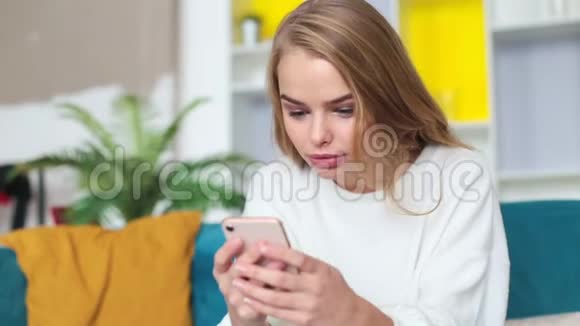 快乐的年轻女子坐在沙发上玩手机赢了视频的预览图