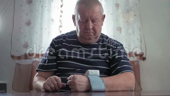 一位老人在家里的桌子上测量血压男性健康检查血压和心率数字视频的预览图