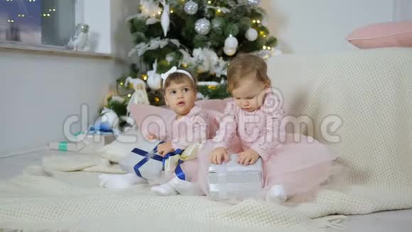 新年礼物可爱的姐妹们坐在地板上在圣诞树的背景下带着礼品盒视频的预览图