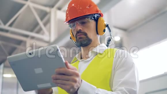关闭一名穿着防护制服的男性工厂工人用他的平板电脑工作视频的预览图