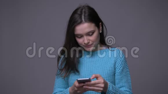 年轻漂亮的深色头发的女性用手机特写镜头微笑着背景与灰色隔离视频的预览图