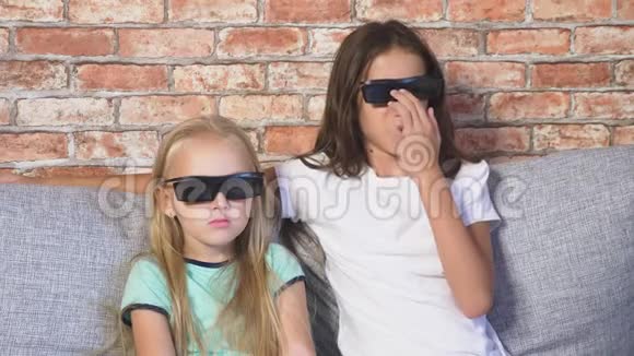 差不多了两个戴着3D眼镜的小女孩坐在客厅的沙发上带着许多情绪看着电影视频的预览图