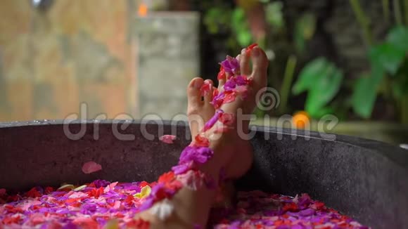 一位美丽的年轻女子在热带水疗中心洗花浴的慢镜头视频的预览图