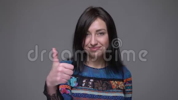 成年白种人深色头发的女性的特写镜头拇指朝上看着灰色背景的摄像机视频的预览图