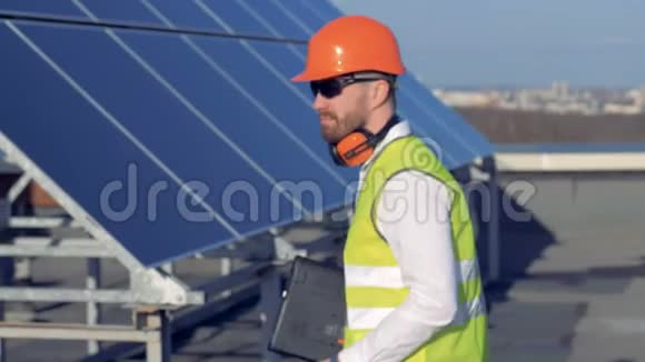 男工人转向相机和微笑而站在屋顶附近的阳光面板4K视频的预览图