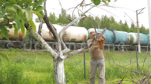 一个人在一棵枯树上砍掉树枝在背景中有一列火车载着一箱石油产品视频的预览图