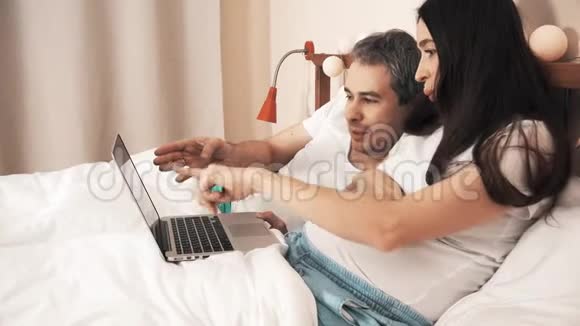 男人和年轻孕妇用笔记本电脑在床上上网购物视频的预览图