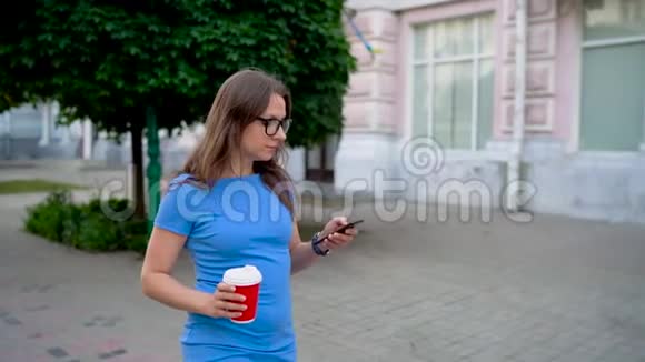 女人在智能手机上说话喝着咖啡走在街上慢动作视频的预览图