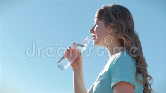 欧洲的女人在露天喝着瓶子里的水对着晴朗的蓝天健康的生活方式视频的预览图