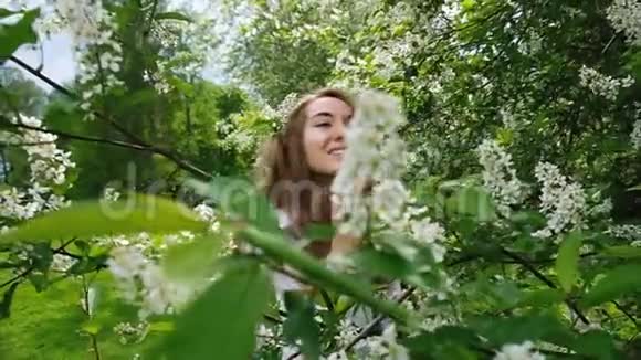 漂亮的欧洲女孩模特在镜头上摆姿势开花的鸟樱桃一个长着蓬松长发和树枝的女人视频的预览图