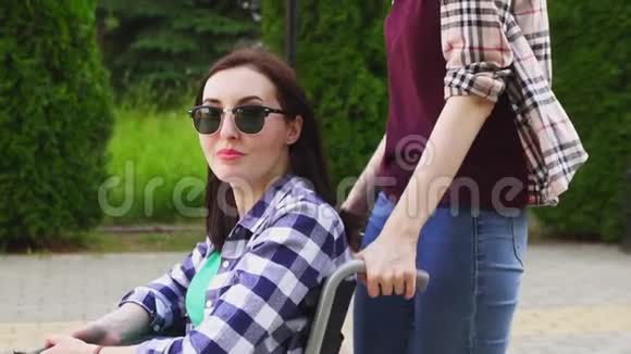 穿衬衫的女孩卷着一个戴眼镜的残疾女孩和一件坐轮椅的衬衫看着摄像机慢节奏视频的预览图