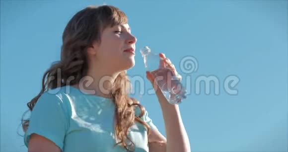 欧洲的女人在露天喝着瓶子里的水对着晴朗的蓝天健康的生活方式视频的预览图