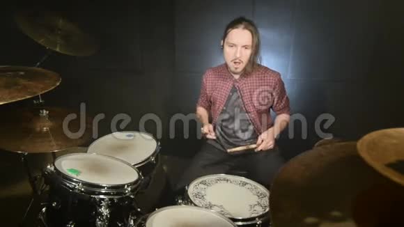 一个长头发的鼓手开始在一个黑色背景的黑暗房间里演奏鼓包摇滚音乐家静态计划视频的预览图