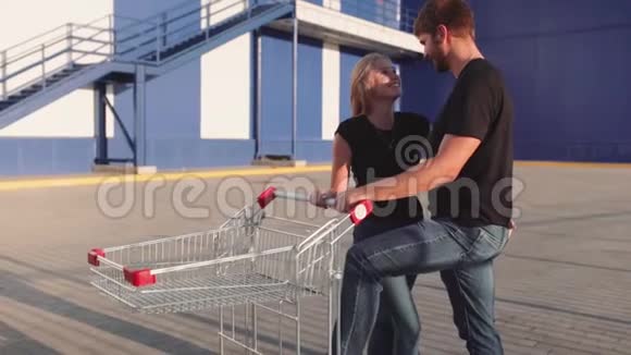 日落时分一对情侣在超市停车场与商店的手推车相爱慢动作视频的预览图