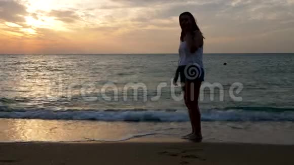 日出时海滩上快乐的女人像个孩子一样在水里跳跃视频的预览图
