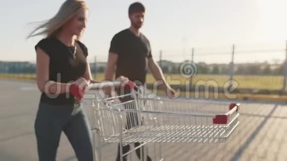 日落时分一对情侣在超市停车场与商店的手推车相爱慢动作视频的预览图