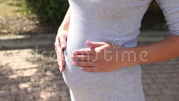 绿树背景下一位身着灰色礼服的孕妇腹部特写视频的预览图