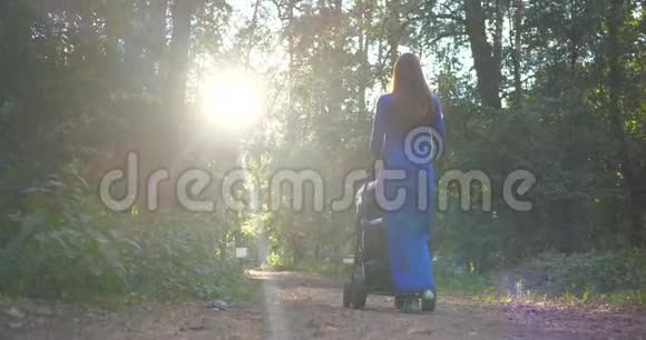 4K慢动作年轻的女人在阳光下和婴儿车在森林里散步视频的预览图