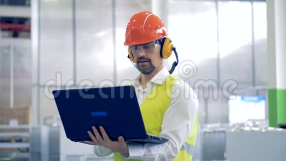 一名男性工厂工人在带笔记本电脑的保护工作服中的工作过程视频的预览图