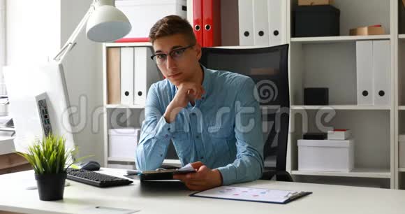 办公室工作人员戴着眼镜坐在桌子旁看着摄像机视频的预览图