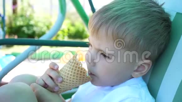 一个小男孩坐在公园的秋千上高兴地吃冰淇淋炎炎夏日冷甜甜点视频的预览图