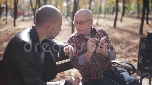 一位年迈的父亲和他成年的儿子坐在公园的长凳上喝咖啡和说话年长父亲的成年儿子视频的预览图