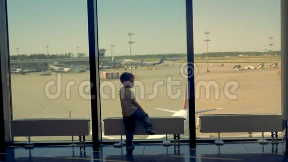 一个男孩在机场休息室玩一个孩子看着相机在机场的窗户附近玩耍视频的预览图