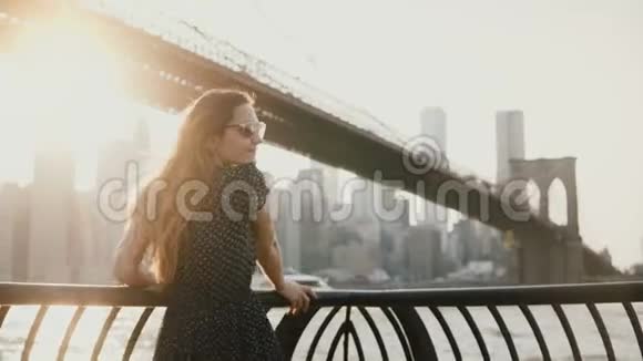 在布鲁克林大桥的河堤围栏上看到一个美丽的女孩她的头发飞扬看着4K摄像机视频的预览图