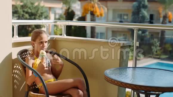 快乐的小女孩穿着黄色泳衣坐在阳台上吃冰淇淋4k视频的预览图