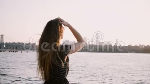后景女孩戴太阳镜独自站在日落海滩上头发在风中吹手臂在空中升起4K视频的预览图