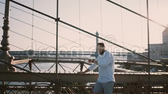 休闲欧洲商人站在布鲁克林大桥使用智能手表手镯然后从相机4K回头视频的预览图