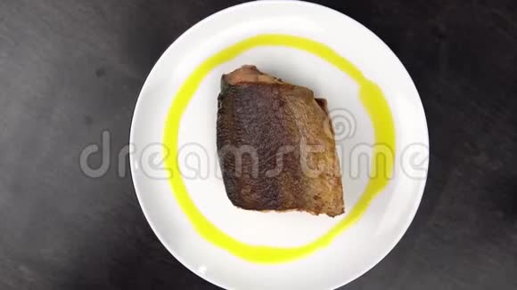 白色盘子上的一片炸红鱼在黑桌上旋转视频的预览图