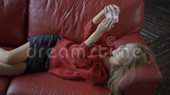 年轻女孩躺在红色沙发上自拍视频的预览图
