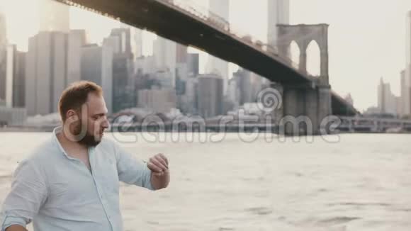 成功的年轻欧洲商人站在布鲁克林大桥下的河边用他的智能手表走开了4K视频的预览图