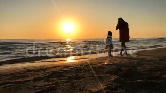 母亲和女儿在日落时沿着海滩散步视频的预览图