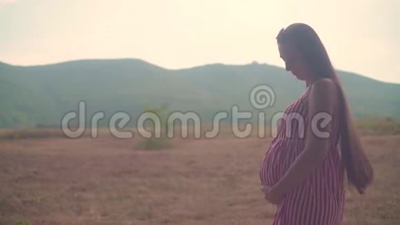 年轻的怀孕迷人的女孩穿着条纹红白连衣裙在晴朗的天气在夏天视频的预览图