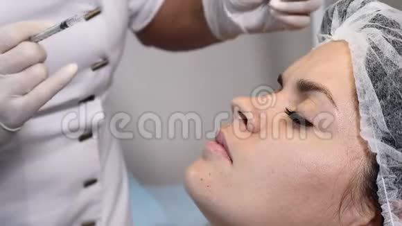 女性整容戴手套的美容师手里拿着一支注射器准备向女性额头注射美容液年轻的视频的预览图