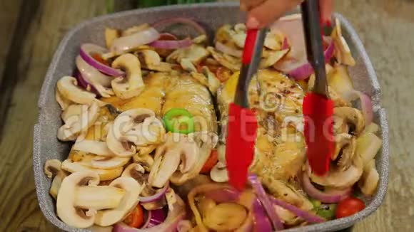 雌性手用火钳转动烤鱼牛排把蘑菇和洋葱混合在一起视频的预览图