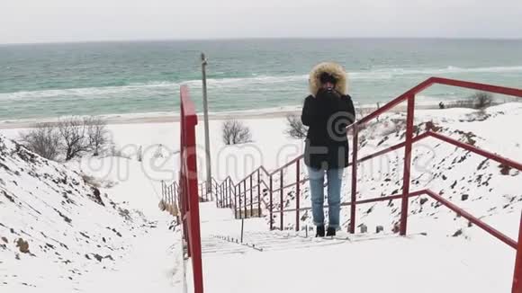 在寒冷的冬天年轻漂亮的女人在大海上拍照慢动作视频的预览图