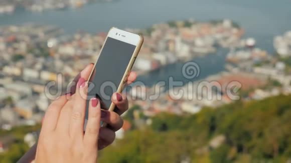 有智能手机的女性手在卑尔根市的背景下使用电话视频的预览图