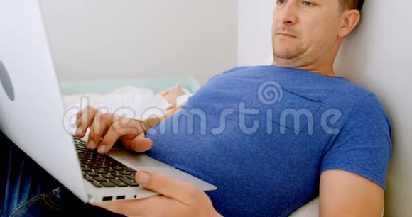 小男孩睡觉父亲在卧室里用笔记本电脑视频的预览图