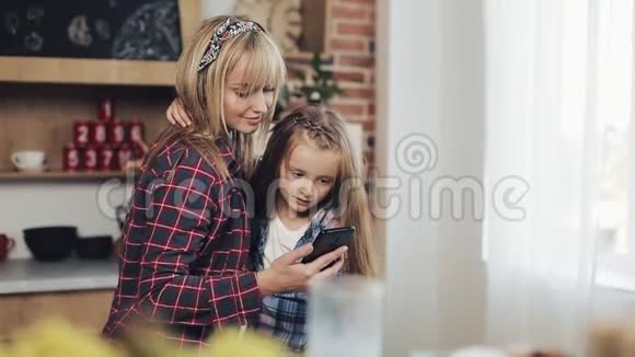快乐的母亲和女儿一起浏览智能手机早上在家厨房微笑视频的预览图