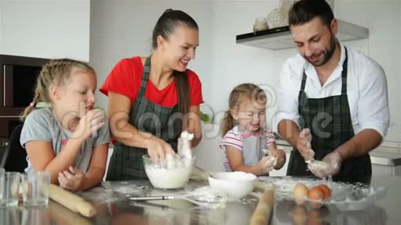 可爱的小女孩和他们美丽的父母在家厨房做饭时揉捏面团和微笑视频的预览图