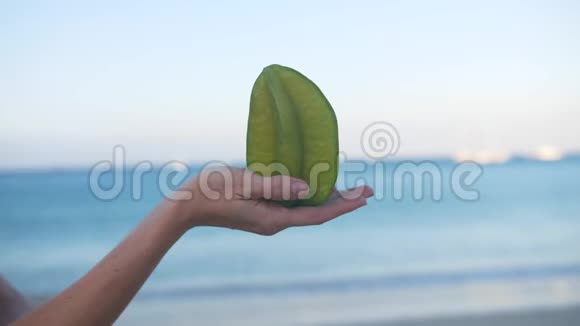 沙滩背景下的雌手握着成熟的星星水果杨桃视频的预览图