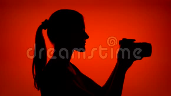 年轻女性的剪影戴上耳机在红色背景下用智能手机听音乐视频的预览图